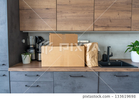 Cardboard box and meal prep kits with fresh ingredients standing on a kitchen countertop. Concept of food delivery service with pre-portioned recipes for easy home cooking. Cardboard box and meal prep kits with fresh ingredients standing on a kitchen countertop. Concept of food delivery service with pre-portioned recipes for easy home cooking. 133619698