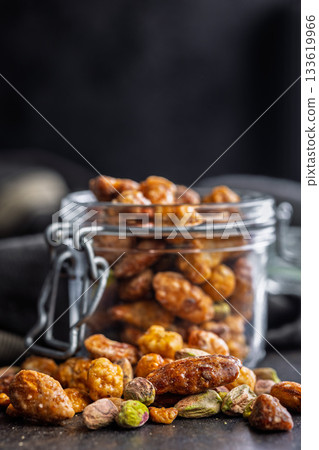 Nuts coated in sugar glaze on black table. 133619966