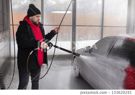 Man in self-service car wash covers red car with foam concentrate Man in self-service car wash covers red car with foam concentrate 133620281