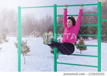 Woman does exercise corner on horizontal bar, pumps abs. Woman does sport in the snow in winter. Woman does exercise corner on horizontal bar, pumps abs. Woman does sport in the snow in winter. 133620283