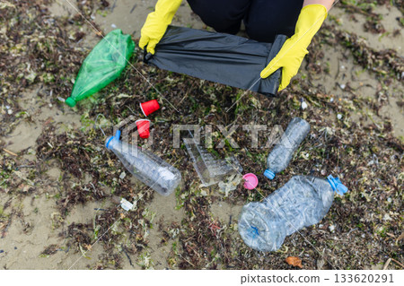 volunteer collecting plastic bottles on a polluted beach, highlighting ocean pollution, waste problem, environmental protection and coastal cleanup action. 133620291