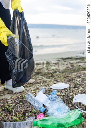 Volunteer collecting plastic waste during beach cleanup, removing litter and protecting the shoreline environment. 133620306