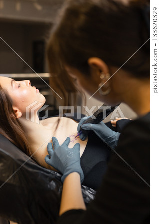 tattoo artist working on a woman chest design in a studio, showing the process of professional tattooing, precision, sterile gloves and cosmetic procedure atmosphere. tattoo artist working on a woman chest design in a studio, showing the process of professional tattooing, precision, sterile gloves and cosmetic procedure atmosphere. 133620329