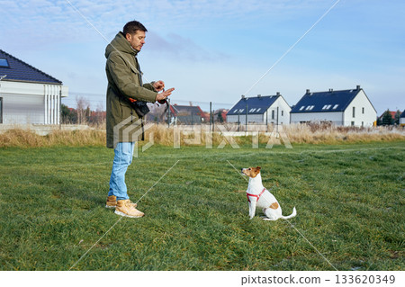 Man standing on grass and training small dog in suburban area Man standing on grass and training small dog in suburban area 133620349