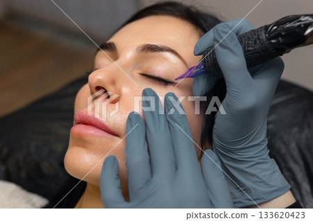 Close up of a cosmetologist performing eyelid permanent makeup, precision eyeliner tattoo procedure with sterile tools, enhancing lash line and eye beauty in a professional studio. Close up of a cosmetologist performing eyelid permanent makeup, precision eyeliner tattoo procedure with sterile tools, enhancing lash line and eye beauty in a professional studio. 133620423