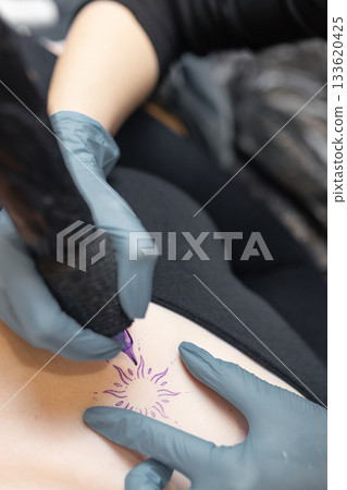 tattoo artist working on a woman chest design in a studio, showing the process of professional tattooing, precision, sterile gloves and cosmetic procedure atmosphere. tattoo artist working on a woman chest design in a studio, showing the process of professional tattooing, precision, sterile gloves and cosmetic procedure atmosphere. 133620425