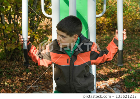 Young Boy Exercising on an Outdoor Fitness Machine in Autumn Park 133621212