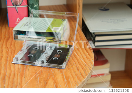 Vintage audio cassette lying among paper books on wooden bookshelf. 133621308