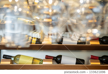 酒架上整齊排列著葡萄酒瓶，前景中擺放著葡萄酒杯。 133621896