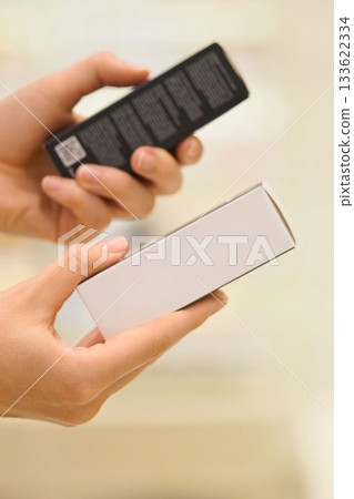 Vertical shot: Woman reading ingredient labels, comparing, choosing between cosmetic products, cream or serum in a beauty store, focusing on packaging and information. The concept of conscious choice. Vertical shot: Woman reading ingredient labels, comparing, choosing between cosmetic products, cream or serum in a beauty store, focusing on packaging and information. The concept of conscious choice. 133622334