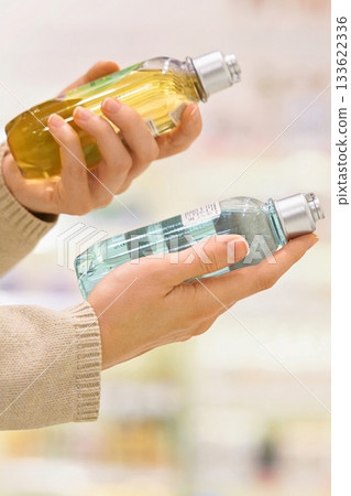 Vertical shot: Woman reading the label of a cosmetic product in a store aisle, focusing on ingredients, with shelves and bottles in the background. Vertical shot: Woman reading the label of a cosmetic product in a store aisle, focusing on ingredients, with shelves and bottles in the background. 133622336