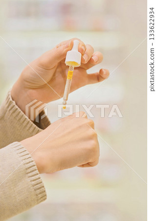 Vertical shot: Woman testing serum texture on her hand before purchase in a beauty store, making an informed choice while selecting a cosmetic product for skincare. Vertical shot: Woman testing serum texture on her hand before purchase in a beauty store, making an informed choice while selecting a cosmetic product for skincare. 133622934