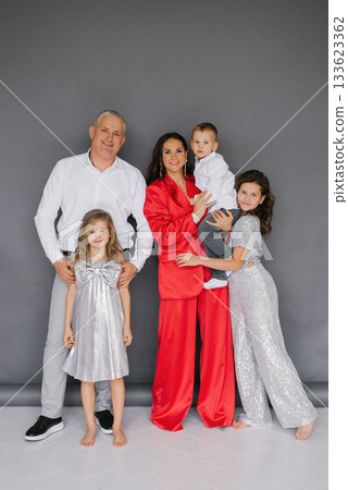 Happy family of five posing for photo, with woman in red suit and a man in white shirt 133623362