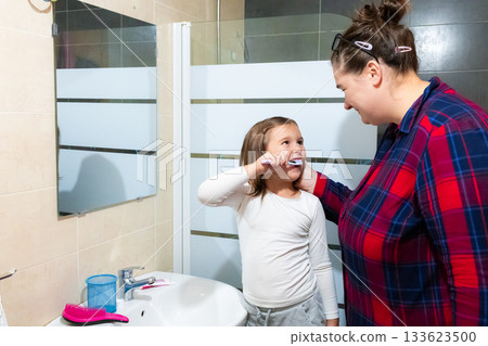 Asian female adult helping asian female child brush teeth in bathroom Asian female adult helping asian female child brush teeth in bathroom 133623500
