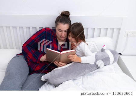 Caucasian female adult reading bedtime story to caucasian female child with stuffed animal on bed Caucasian female adult reading bedtime story to caucasian female child with stuffed animal on bed 133623605