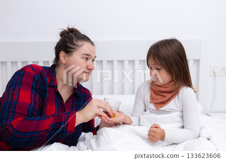 Mother giving medicine to daughter in bed during illness Mother giving medicine to daughter in bed during illness 133623606