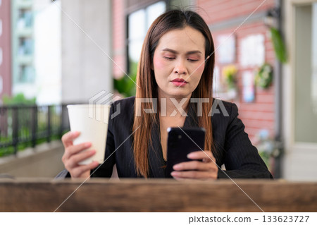 Professional Asian Thai Business Woman Outdoors Drinking Coffee and Using Phone Professional Asian Thai Business Woman Outdoors Drinking Coffee and Using Phone 133623727