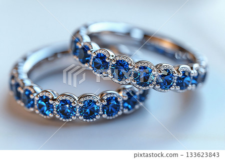 Luxurious pair of wedding rings with blue stones on a white background. Rococo-Renaissance style. 133623843