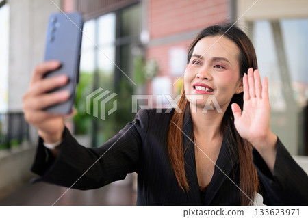 Happy Thai Business Woman Outdoors in Professional Attire Having Video Call Meeting with Phone Happy Thai Business Woman Outdoors in Professional Attire Having Video Call Meeting with Phone 133623971