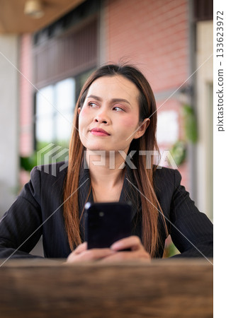 Thai Business Woman Outdoors in Professional Attire Using Phone and Thinking Thai Business Woman Outdoors in Professional Attire Using Phone and Thinking 133623972
