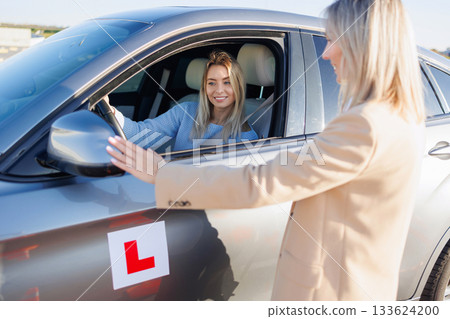 Driving Instructor Checking Exterior Mirrors of Learner Vehicle Before Test 133624200