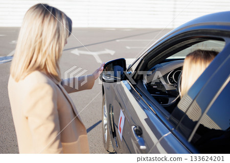 Instructor Adjusting Side Mirror for Student Driver before Driving Lesson 133624201
