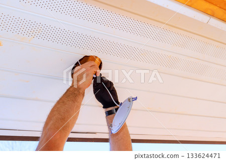 Worker is fitting light fixture to ceiling outdoors, focusing on careful installation safety. Worker is fitting light fixture to ceiling outdoors, focusing on careful installation safety. 133624471