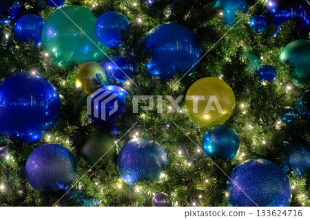 Blue, teal, and green baubles fill a Christmas tree lit with twinkle lights. The cool tones and reflections create a rich festive texture. 133624716