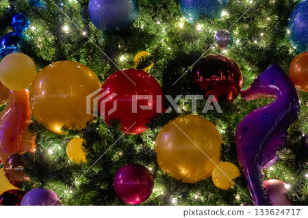 A purple seahorse and glossy baubles decorate a Christmas tree at night. Warm lights glow through green branches for a vibrant festive close-up. A purple seahorse and glossy baubles decorate a Christmas tree at night. Warm lights glow through green branches for a vibrant festive close-up. 133624717
