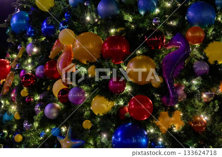 Yellow and purple seahorses sit among shiny baubles and twinkle lights on a Christmas tree. The marine decorations add a fun, colorful holiday style. Yellow and purple seahorses sit among shiny baubles and twinkle lights on a Christmas tree. The marine decorations add a fun, colorful holiday style. 133624718