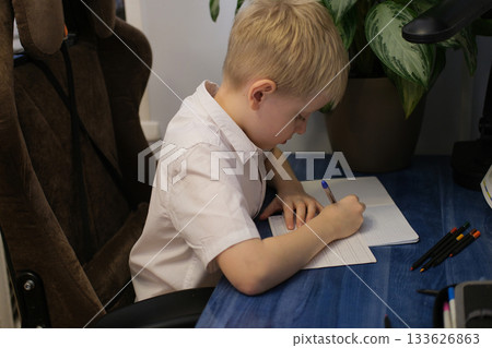 Young boy studying writing homework at blue desk 133626863