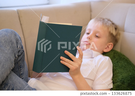 Young boy reading book on couch learning at home Young boy reading book on couch learning at home 133626875