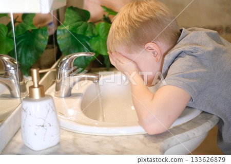 Young boy washing face in bathroom sink during morning routine Young boy washing face in bathroom sink during morning routine 133626879