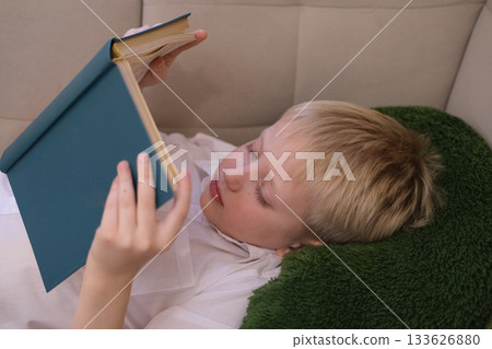 Relaxed young boy reading a book indoors Relaxed young boy reading a book indoors 133626880