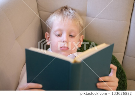 Young boy learning by reading book in armchair Young boy learning by reading book in armchair 133626882