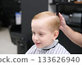 Blond boy getting stylish haircut in barbershop 133626940