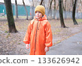 Child wearing orange raincoat during autumn weather outdoors 133626942