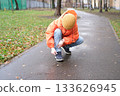 Person crouching tying shoelace on wet autumn park path 133626945