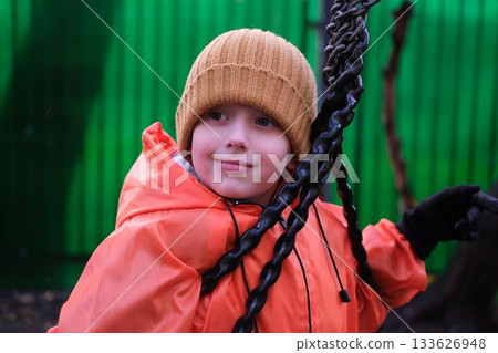Young boy smiling playing on playground swing 133626948