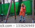 Child playing on swing in orange raincoat 133626949