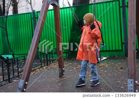 Child playing on swing in orange raincoat Child playing on swing in orange raincoat 133626949