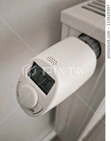 Digital thermostat on a white radiator with LOC and day of the week indicator. Side view. 133626997