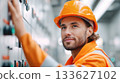Male technician in orange safety gear is operating control panel in industrial setting, showcasing expertise and focus on electrical systems 133627102