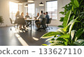 Group of professionals engaged in a collaborative meeting around a conference table, with lush greenery and warm sunlight enhancing the atmosphere 133627110