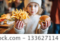 Child holding delicious burger and crispy fries in cozy restaurant setting, showcasing joyful dining experience with family and friends 133627114
