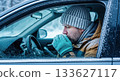 Man sitting in car during winter, warming hands with breath visible, surrounded by snow-covered landscape, conveying cold weather challenges 133627117