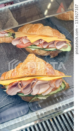 Freshly made savory croissant sandwiches with ham, cheese, tomato, and cucumber in a refrigerated display Freshly made savory croissant sandwiches with ham, cheese, tomato, and cucumber in a refrigerated display 133627187