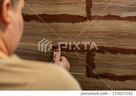 A man applies grout to the joints of wood-look ceramic tiles during a home renovation A close-up of his hands smoothing the grout for a clean, professional finish on the floor or walls inside a room. A man applies grout to the joints of wood-look ceramic tiles during a home renovation A close-up of his hands smoothing the grout for a clean, professional finish on the floor or walls inside a room. 133627192