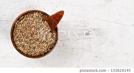Unpeeled hemp - Cannabis sativa - in small dark wooden bowl on white stone board desk, empty space for text right side Unpeeled hemp - Cannabis sativa - in small dark wooden bowl on white stone board desk, empty space for text right side 133628145