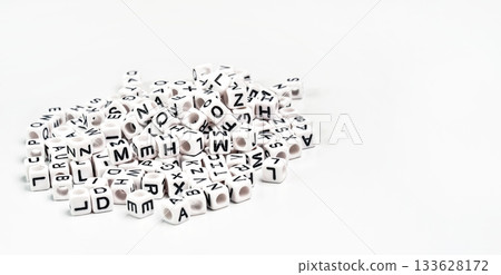 Heap of small white cube beads with various letters scattered on board, space for text right side 133628172